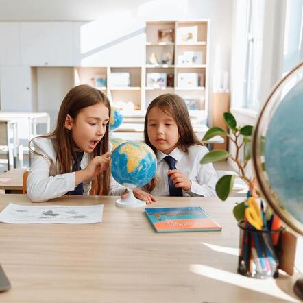 Picture of two girls in a classroom studying a globe.